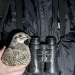 A sage grouse held tucked under the arm of person wearing a dark weather resistant jacket